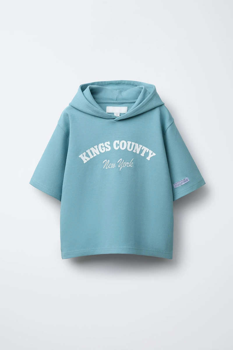 SWEAT À MANCHES COURTES, CAPUCHE ET INSCRIPTION