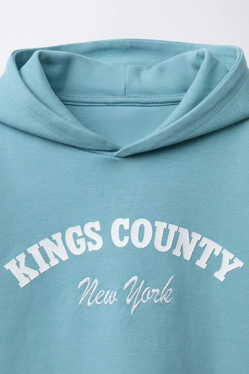 SWEAT À MANCHES COURTES, CAPUCHE ET INSCRIPTION