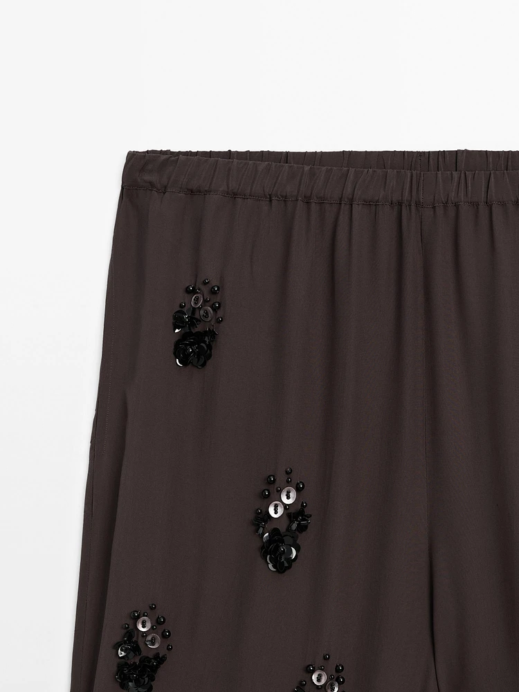 Flowing trousers with floral appliqués