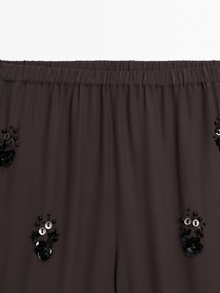 Flowing trousers with floral appliqués