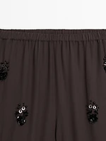 Flowing trousers with floral appliqués