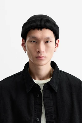 Hat made of tonal matching fabrics with turned-up knit brim. Adjusts with loop.