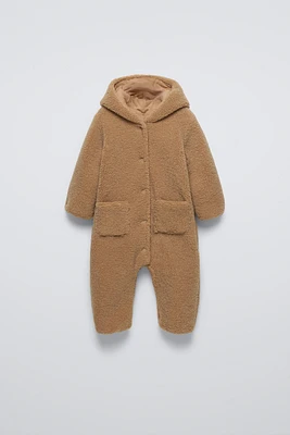 Faux shearling bodysuit with hood and long sleeves. Snap button closure front patch pockets.Interior lining.