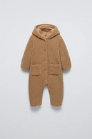 Faux shearling bodysuit with hood and long sleeves. Snap button closure front patch pockets.Interior lining.