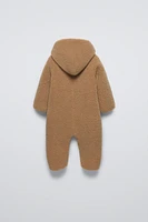 Faux shearling bodysuit with hood and long sleeves. Snap button closure front patch pockets.Interior lining.