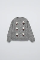 Knit sweater with round neck and long sleeves. Embroidered flower detail on front