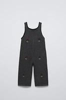 Sleeveless knit overalls with round neckline. Front floral embroidered detail.