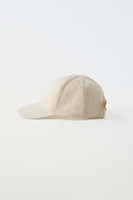 Hat with adjustable adhesive strap at nape.