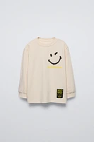 Crew neck T-shirt. Cuffed long sleeves. Smileyworld ® print at front and back. Label appliqué hem.