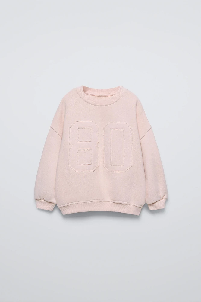 Round neck sweatshirt with long sleeves. Rib trim. Front embroidered patch detail.