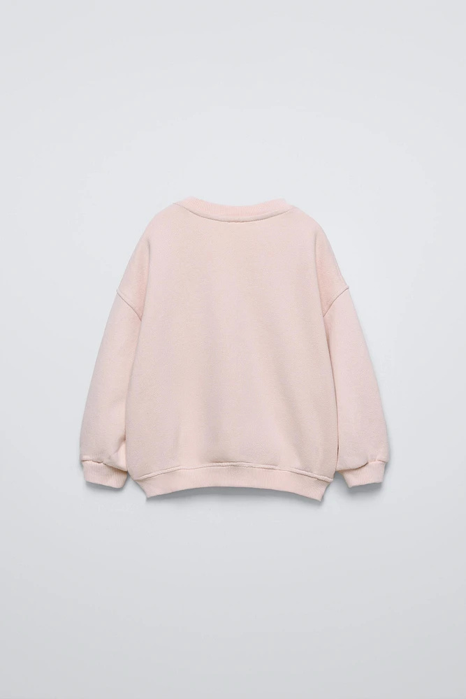 Round neck sweatshirt with long sleeves. Rib trim. Front embroidered patch detail.