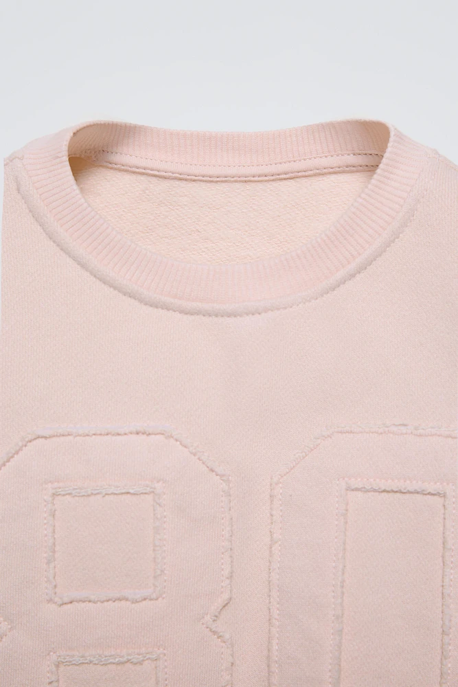 Round neck sweatshirt with long sleeves. Rib trim. Front embroidered patch detail.