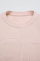 Round neck sweatshirt with long sleeves. Rib trim. Front embroidered patch detail.