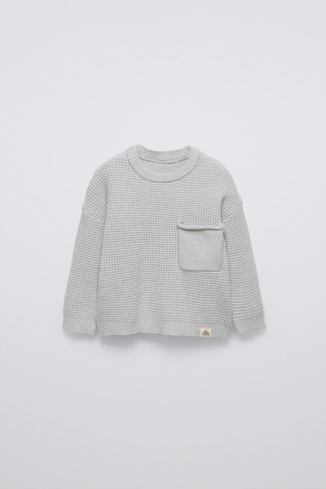 Sweater with round neck and long sleeves cuffs. Back button closure. Patch pocket at chest. Label appliqué hem.