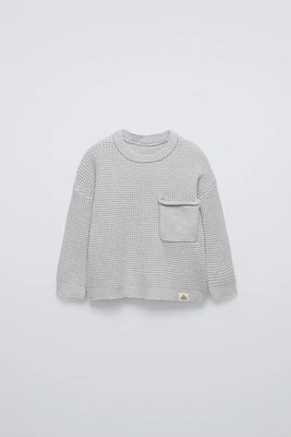 Sweater with round neck and long sleeves cuffs. Back button closure. Patch pocket at chest. Label appliqué hem.