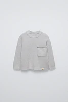 Sweater with round neck and long sleeves cuffs. Back button closure. Patch pocket at chest. Label appliqué hem.