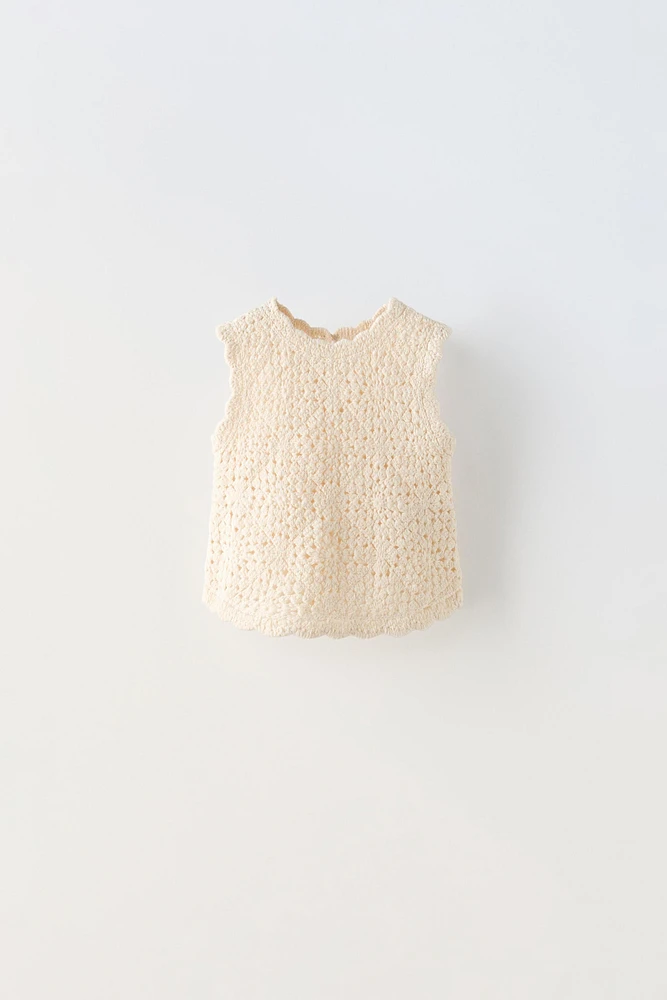 Sleeveless round neck knit top. Buttoned teardrop closure at back.