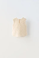 Sleeveless round neck knit top. Buttoned teardrop closure at back.