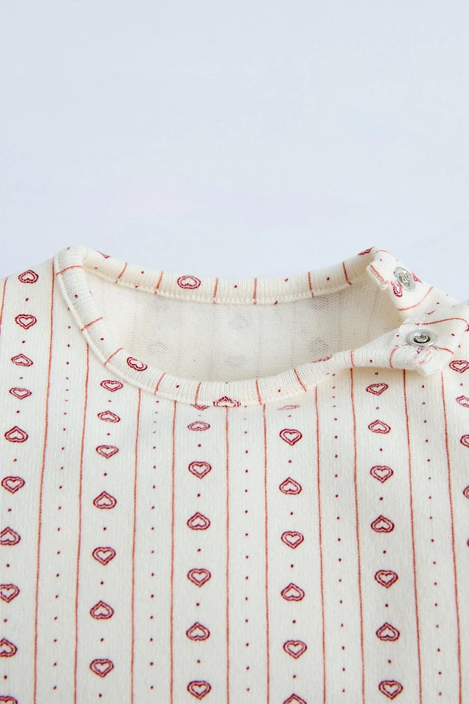 Round neck shirt with long sleeves. Snap button closure at shoulder. Hearts print and warm fabric.