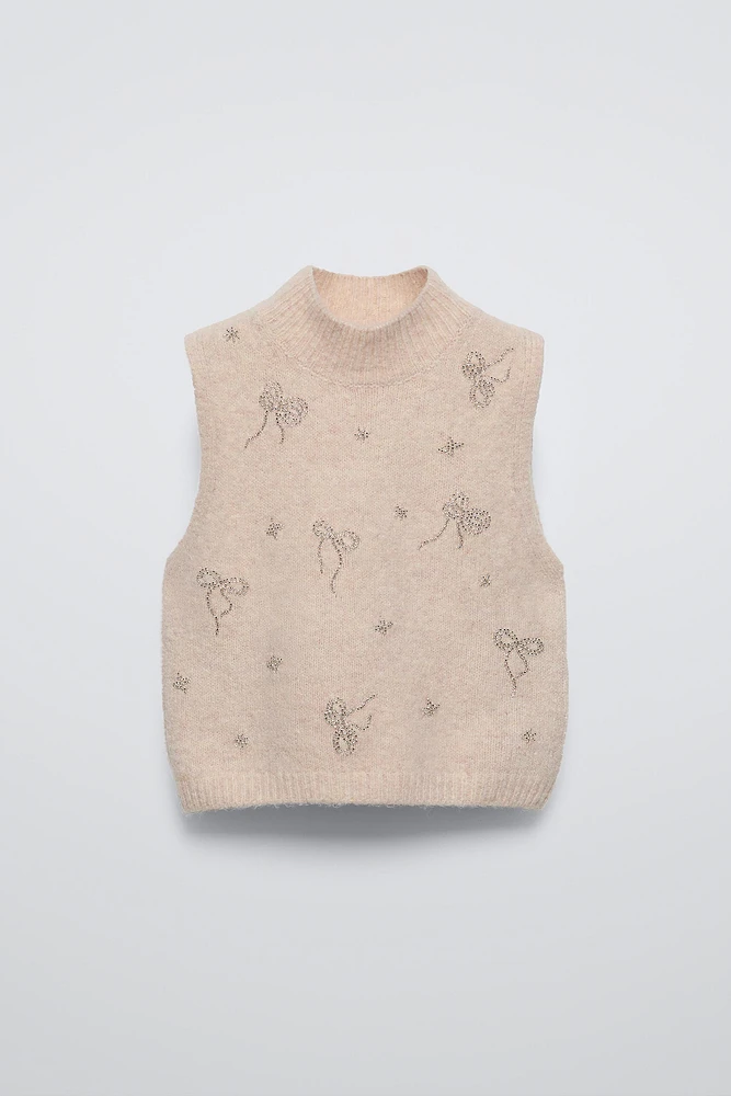 High collar knit vest. Bow shaped beading appliqués at front.