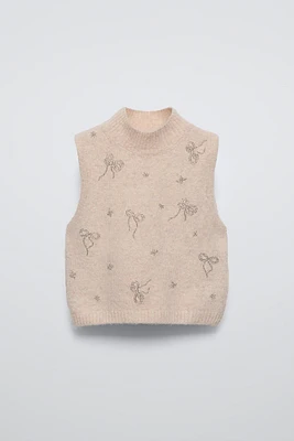 High collar knit vest. Bow shaped beading appliqués at front.