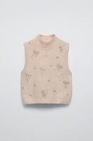 High collar knit vest. Bow shaped beading appliqués at front.