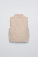 High collar knit vest. Bow shaped beading appliqués at front.