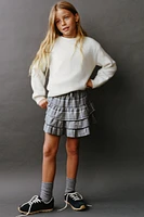 Skirt with elastic waistband and front drawstring appliqués. Ruffle detail plaid print.