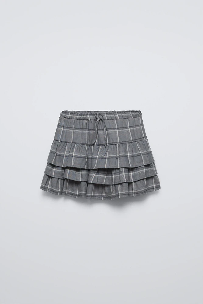 Skirt with elastic waistband and front drawstring appliqués. Ruffle detail plaid print.