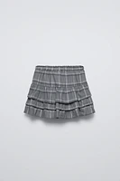 Skirt with elastic waistband and front drawstring appliqués. Ruffle detail plaid print.