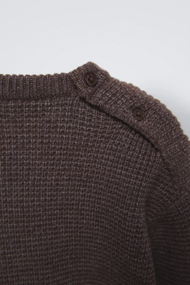 Sweater with round neck and long sleeves cuffs. Back button closure. Patch pocket at chest. Label appliqué hem.