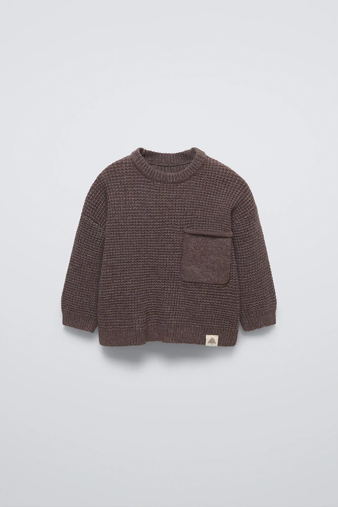 Sweater with round neck and long sleeves cuffs. Back button closure. Patch pocket at chest. Label appliqué hem.